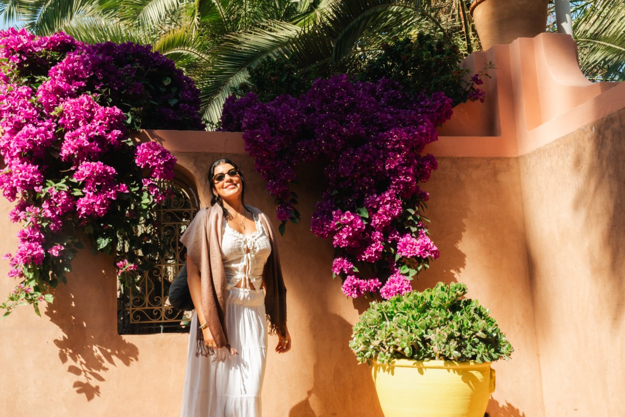 Young female solo traveller on a group tour poses in front of a flower wall in Jardin Majorelle in Morocco 