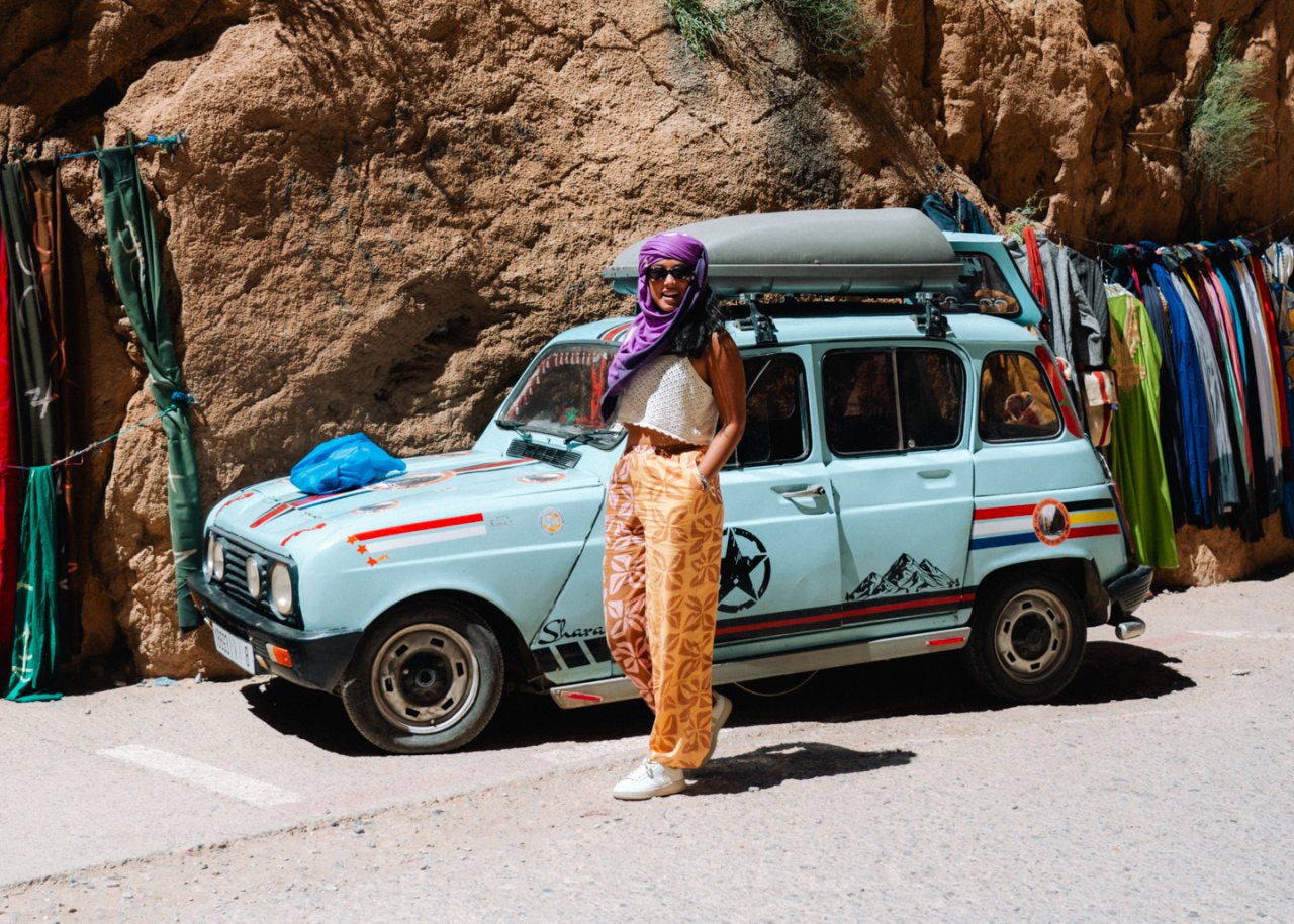 Young female travellers poses in front of a locals car in the middle of Todra Gorge in Morocco. 